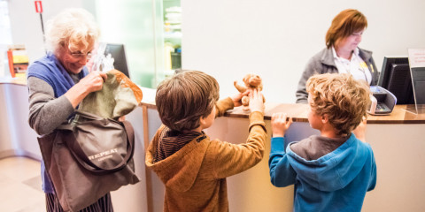 Twee kinderen en hun grootmoeder staan bij de kassa van het museum