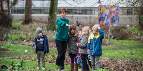 Een gids geeft uitleg aan een klein groepje kinderen in de plantentuin van het museum