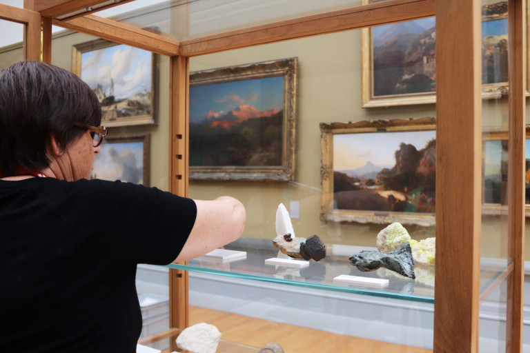 Een medewerker van De wereld van Kina schikt stukken in een vitrinekast, in een museumzaal van het MSK